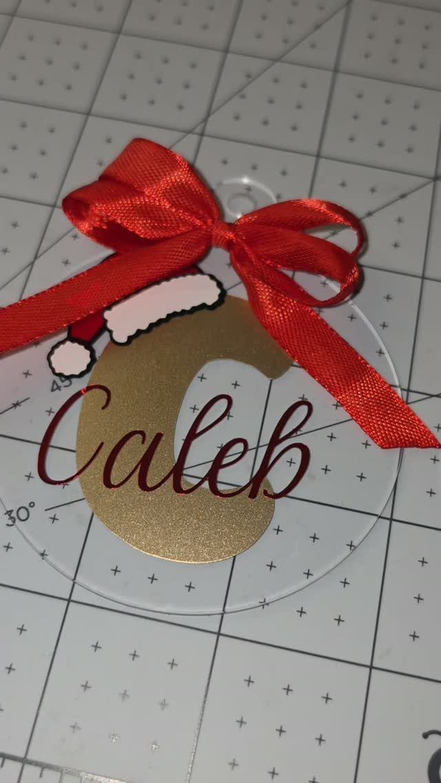 Clear circular ornament with gold initial C, red name Caleb, and red bow.