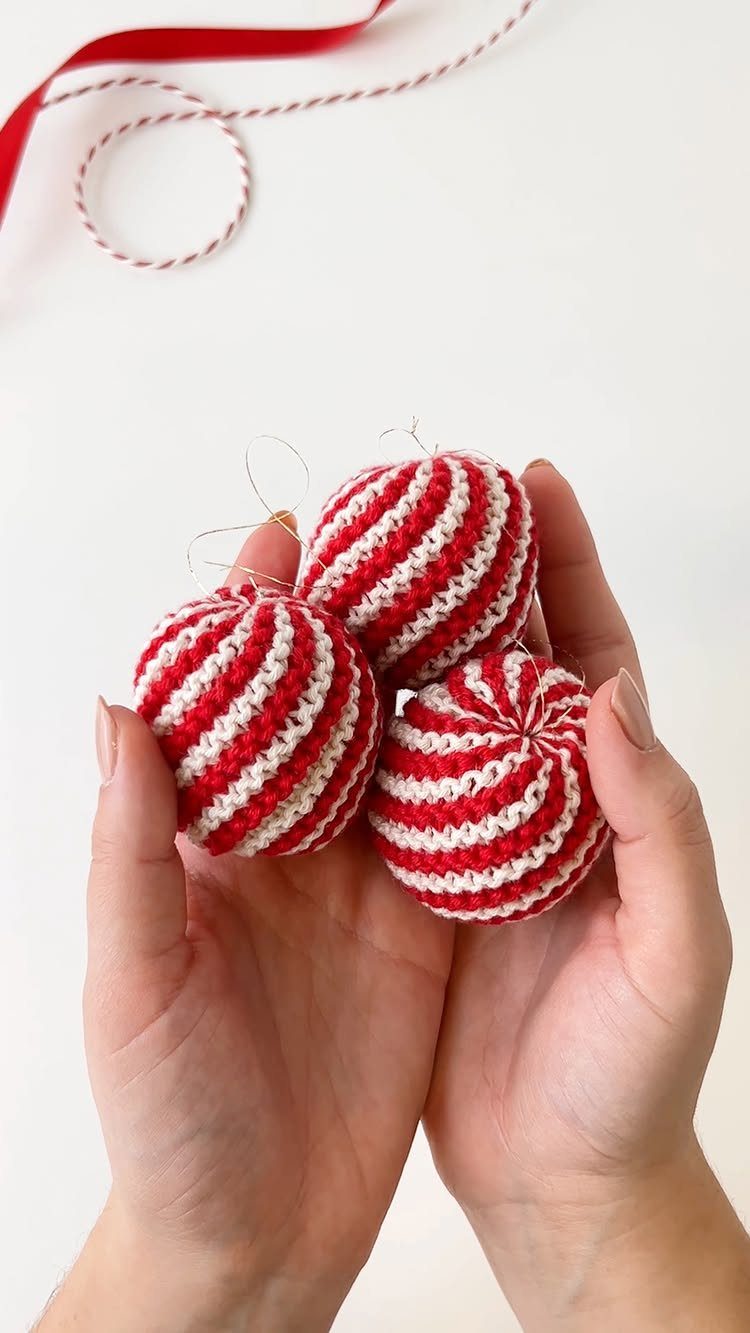 Three red and white striped crocheted peppermint baubles held in two hands.