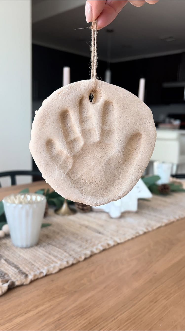 Circular salt dough ornament with a handprint impression hanging from a twine string.