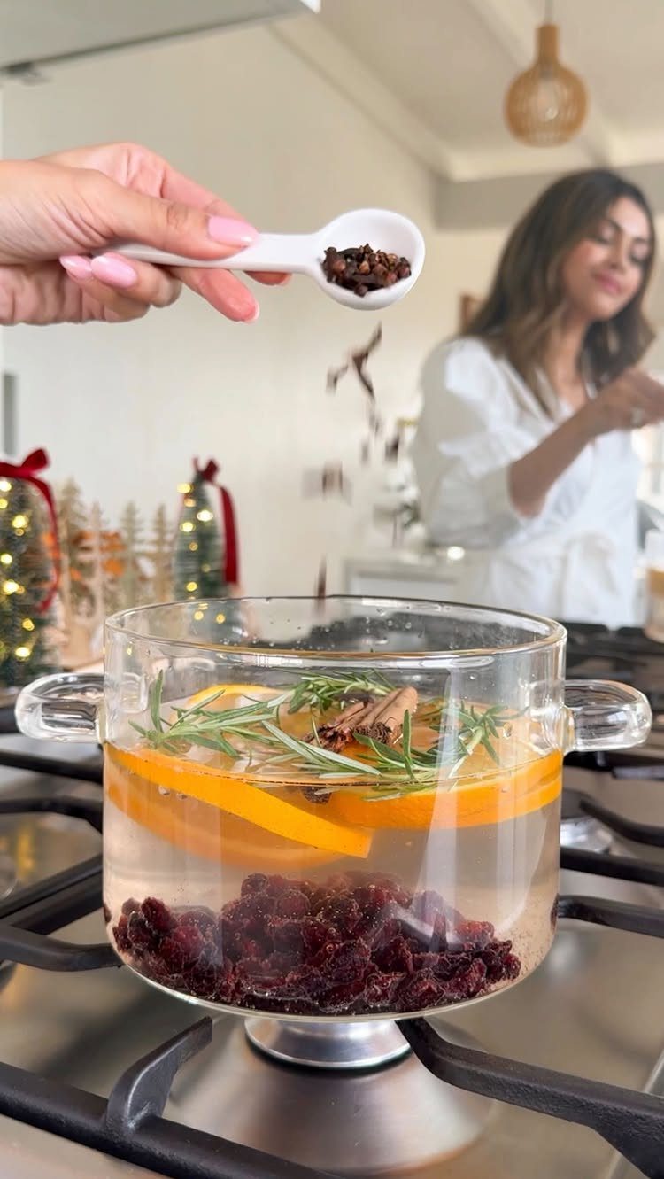 Dried cloves being added to a pot of simmering orange and cinnamon potpourri.