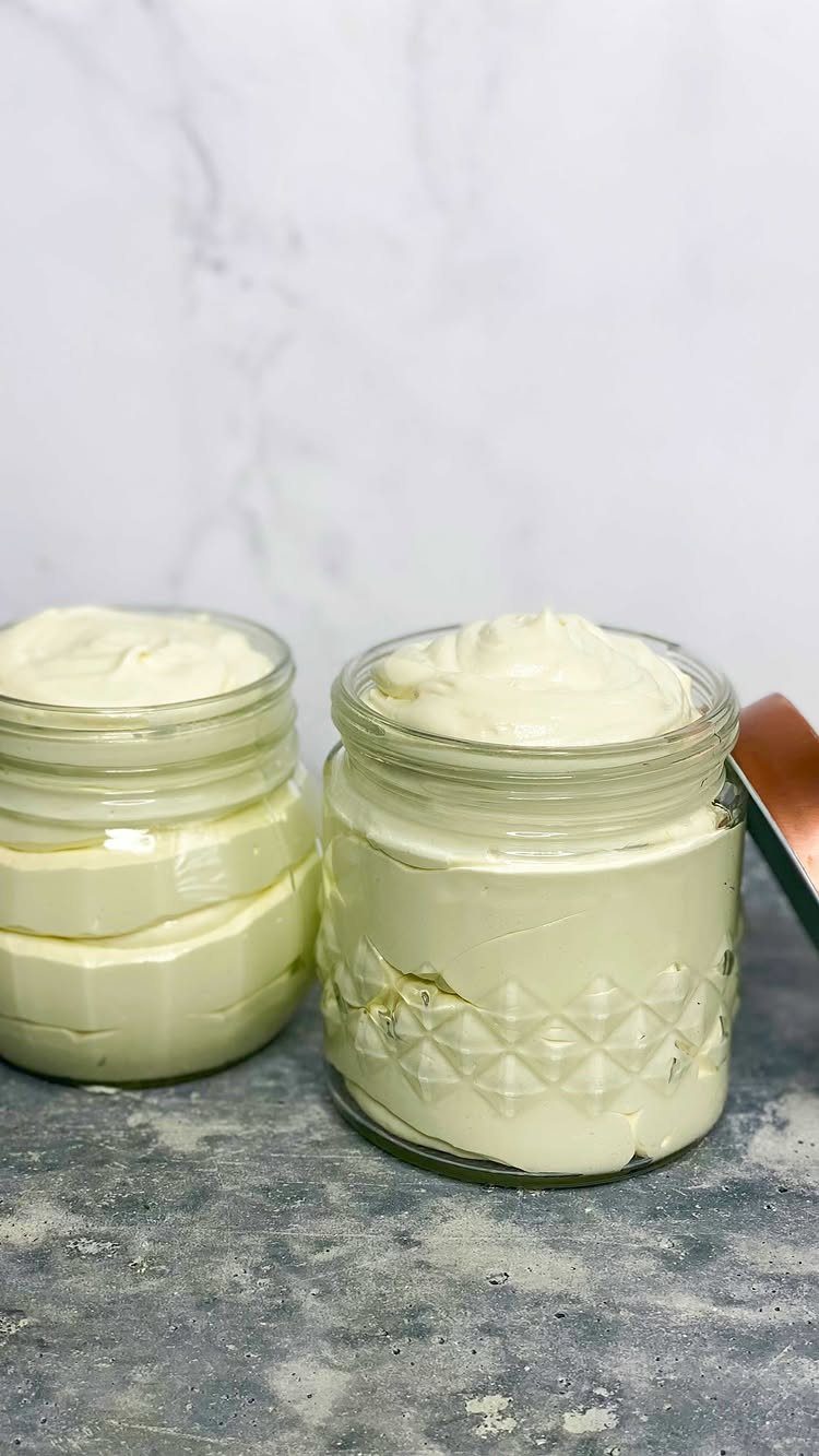 Two glass jars filled with creamy white whipped body butter on a grey surface.