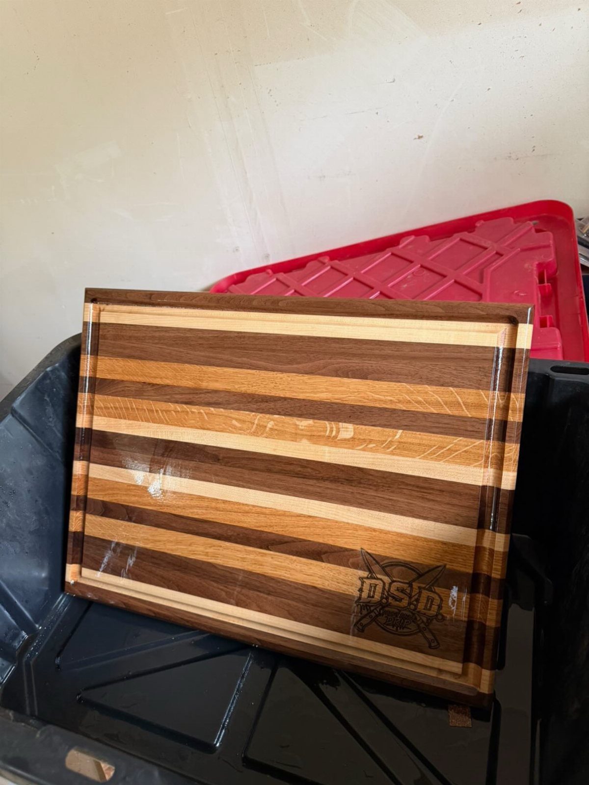 Striped wooden cutting board with an engraved logo leaning against plastic bins.