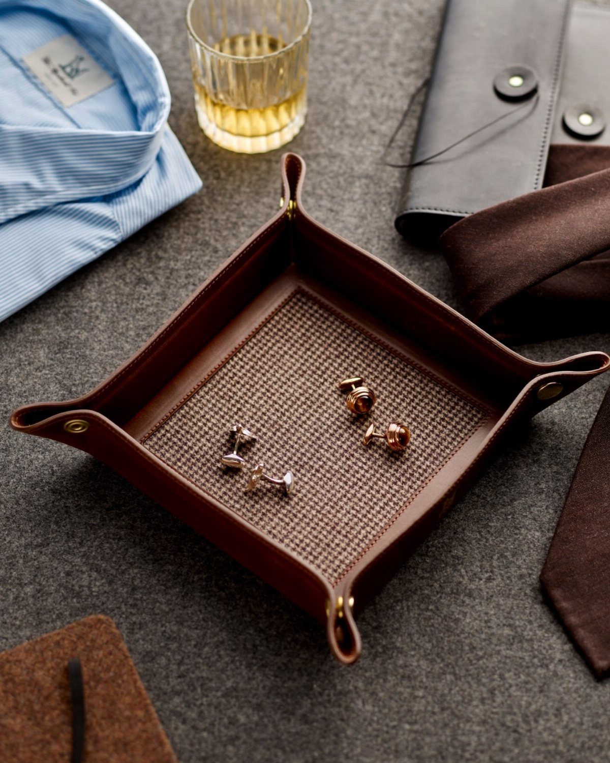 Brown leather catchall tray holding cufflinks next to a shirt and tie.