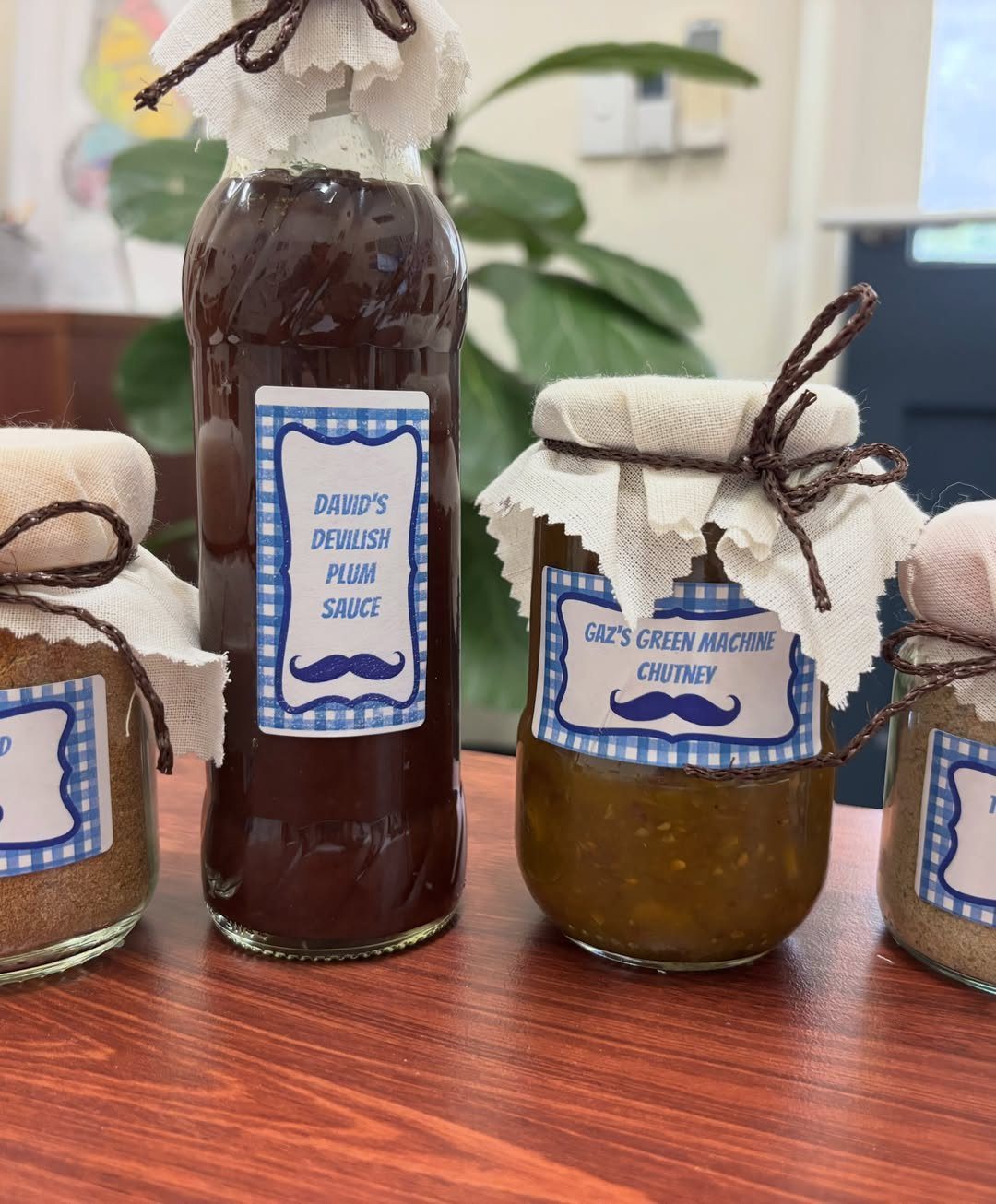Homemade sauces and chutneys in glass jars with blue checkered mustache labels.