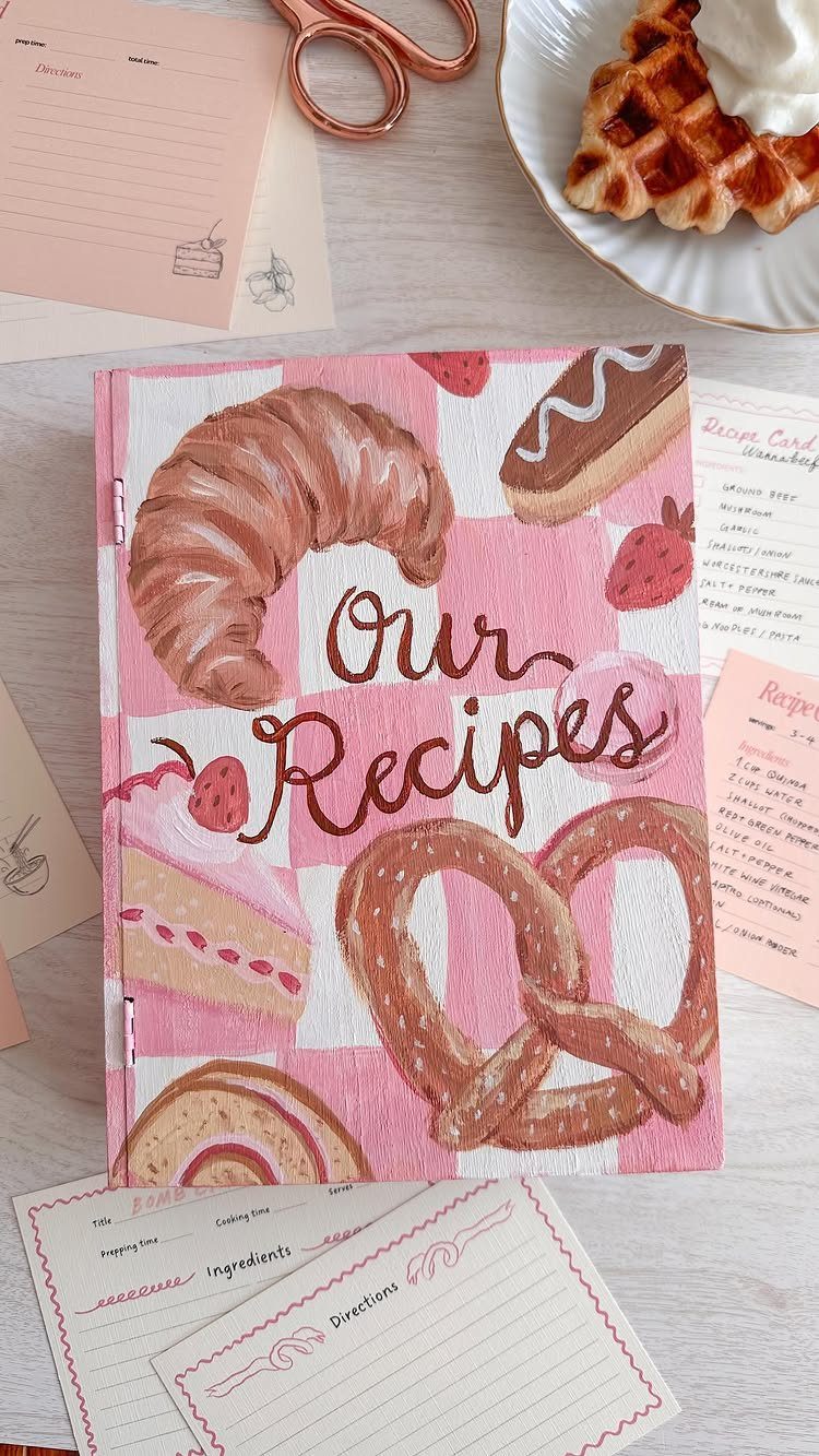 Pink checkered recipe booklet with food illustrations surrounded by recipe cards and waffles.