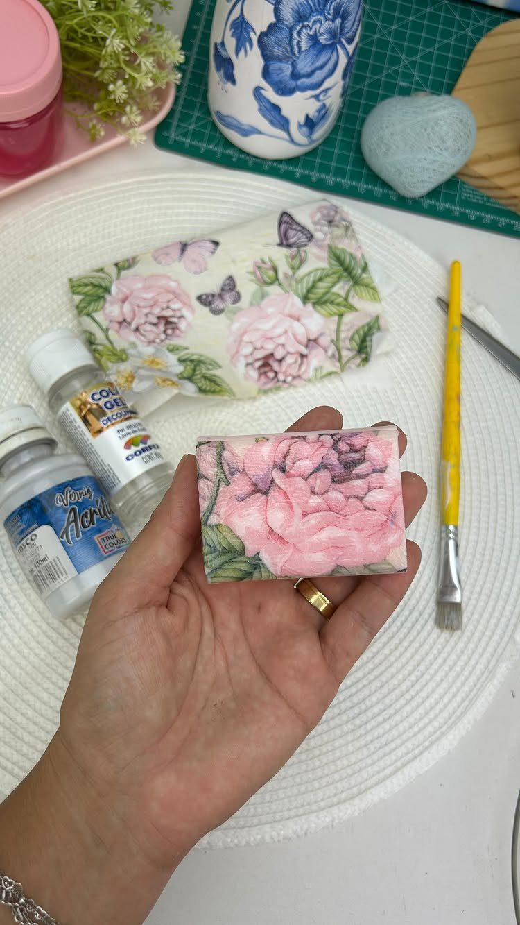Hand holding a bar of soap decorated with pink floral decoupage patterns.