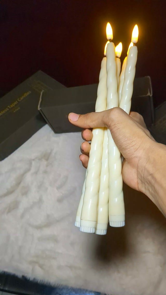 Hand holding a bundle of lit white twisted taper candles against dark background