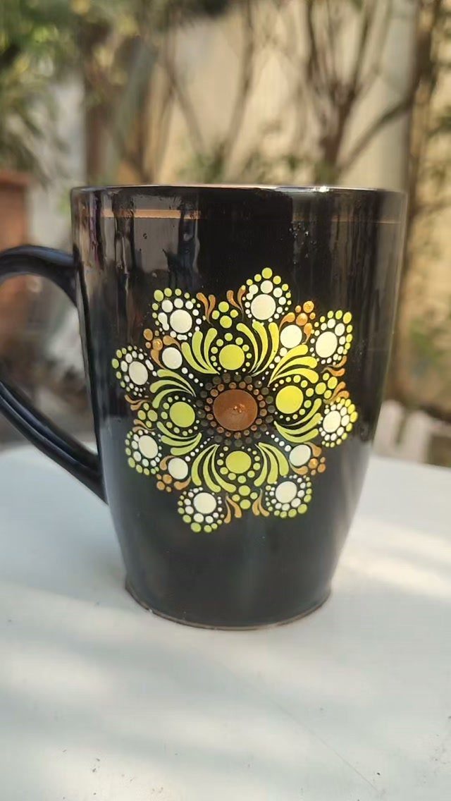 Black ceramic mug with a hand-painted yellow and white mandala floral design.