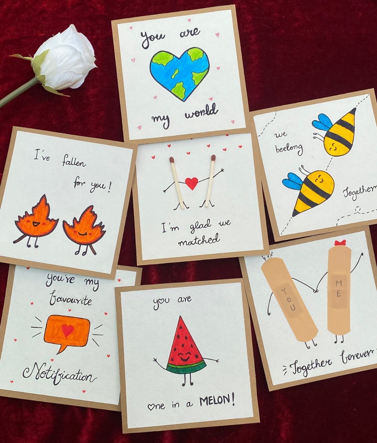 Handmade pun cards with cute drawings arranged on red velvet with a white rose.