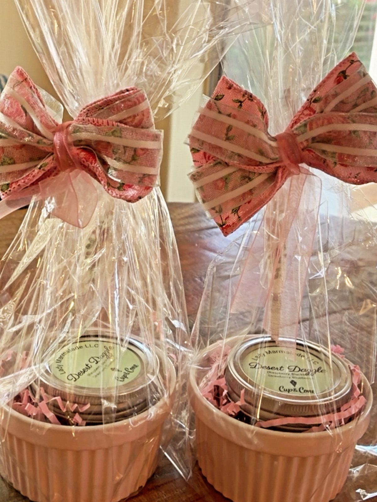 Two jars of preserves in pink ramekins wrapped in cellophane with floral bows.