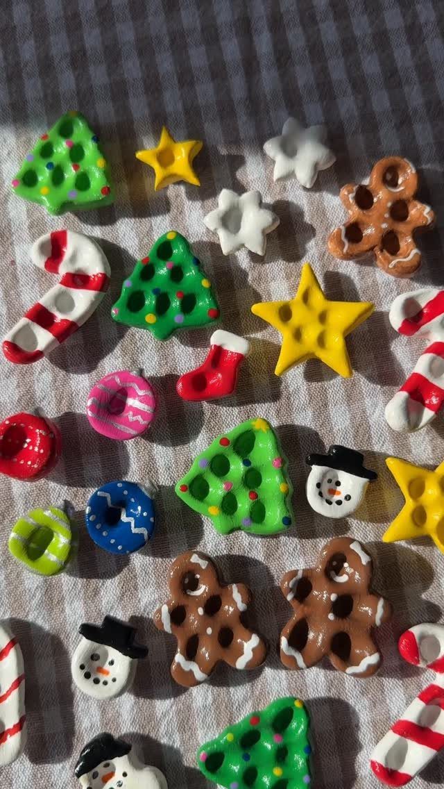 Colorful polymer clay Christmas charms scattered on a grey checkered fabric background.