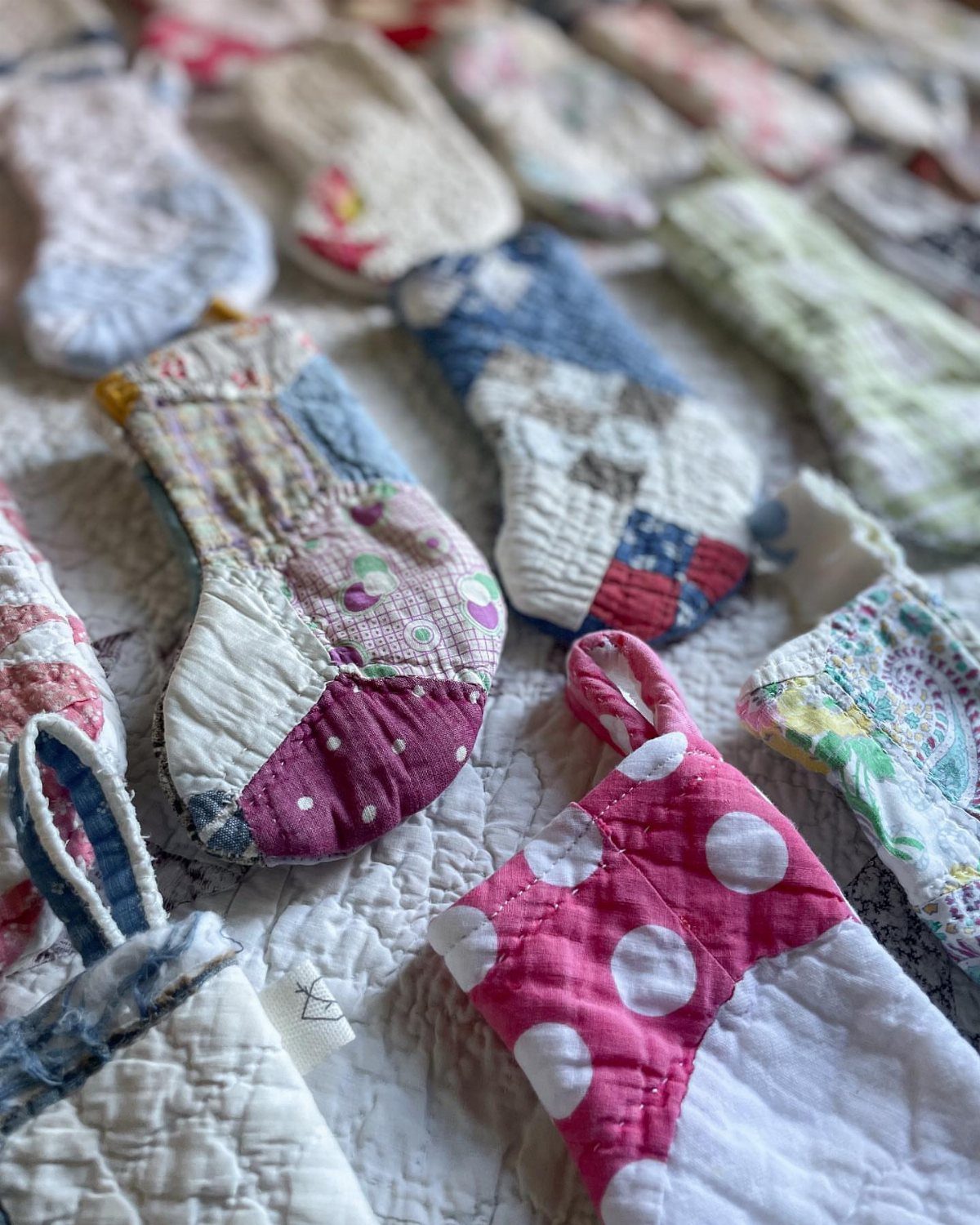 Handmade quilted pot holders and oven mitts in colorful patterns on white fabric.