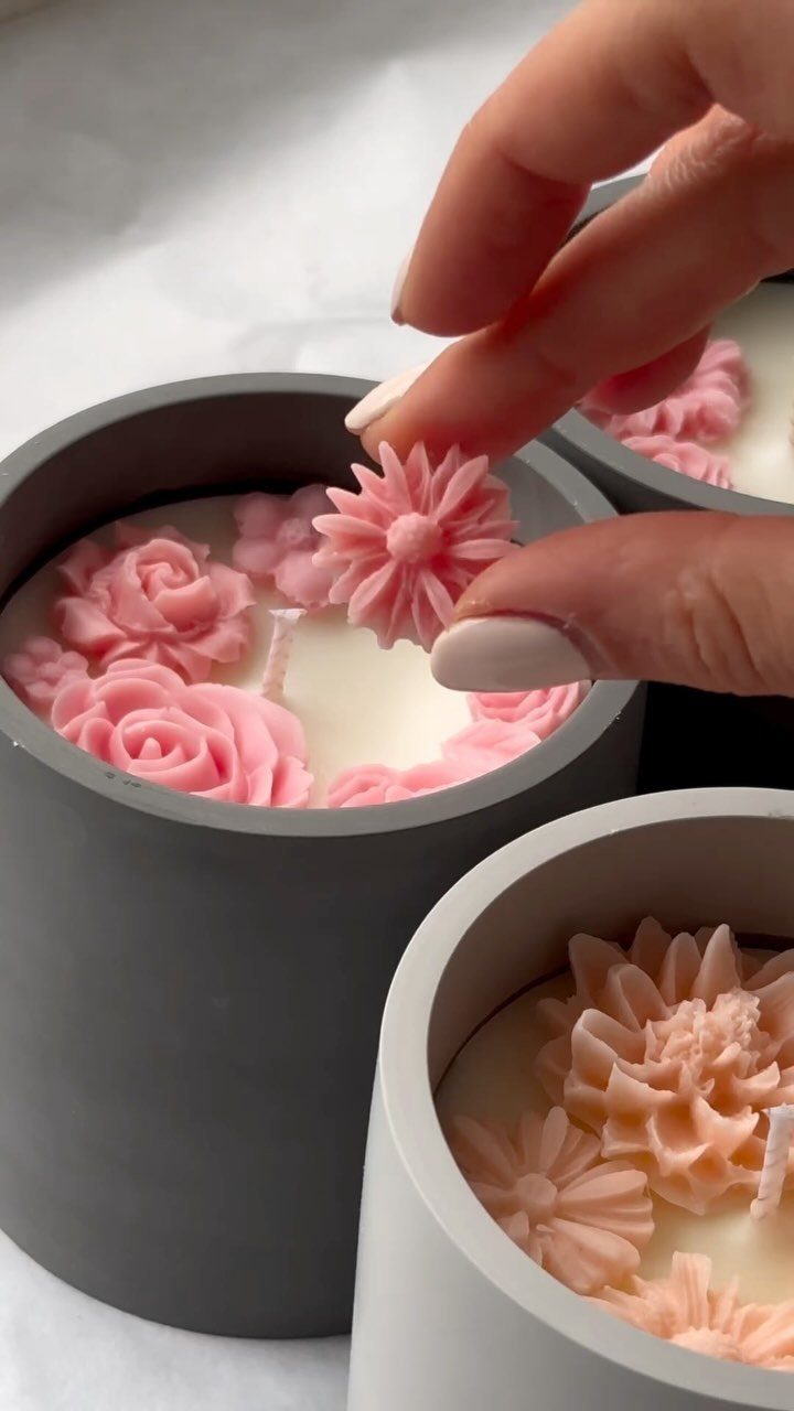 Hand placing pink wax flowers onto a white candle in a grey container