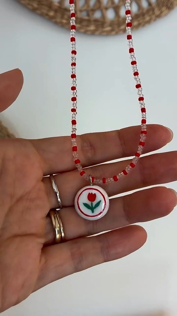 Hand holding a beaded necklace with a white clay tulip pendant.