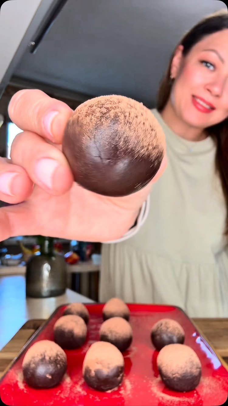 Chocolate truffles dusted with cocoa powder on a red plate and held by hand.