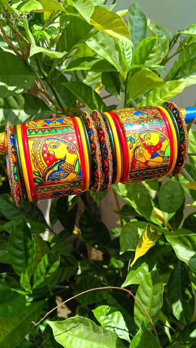 Painted colorful bangles with traditional designs resting on a branch among green leaves.