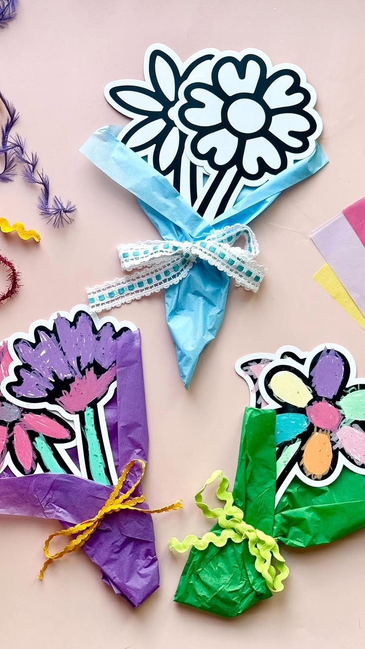 Three paper flower bouquets wrapped in colorful tissue paper on a pink surface.