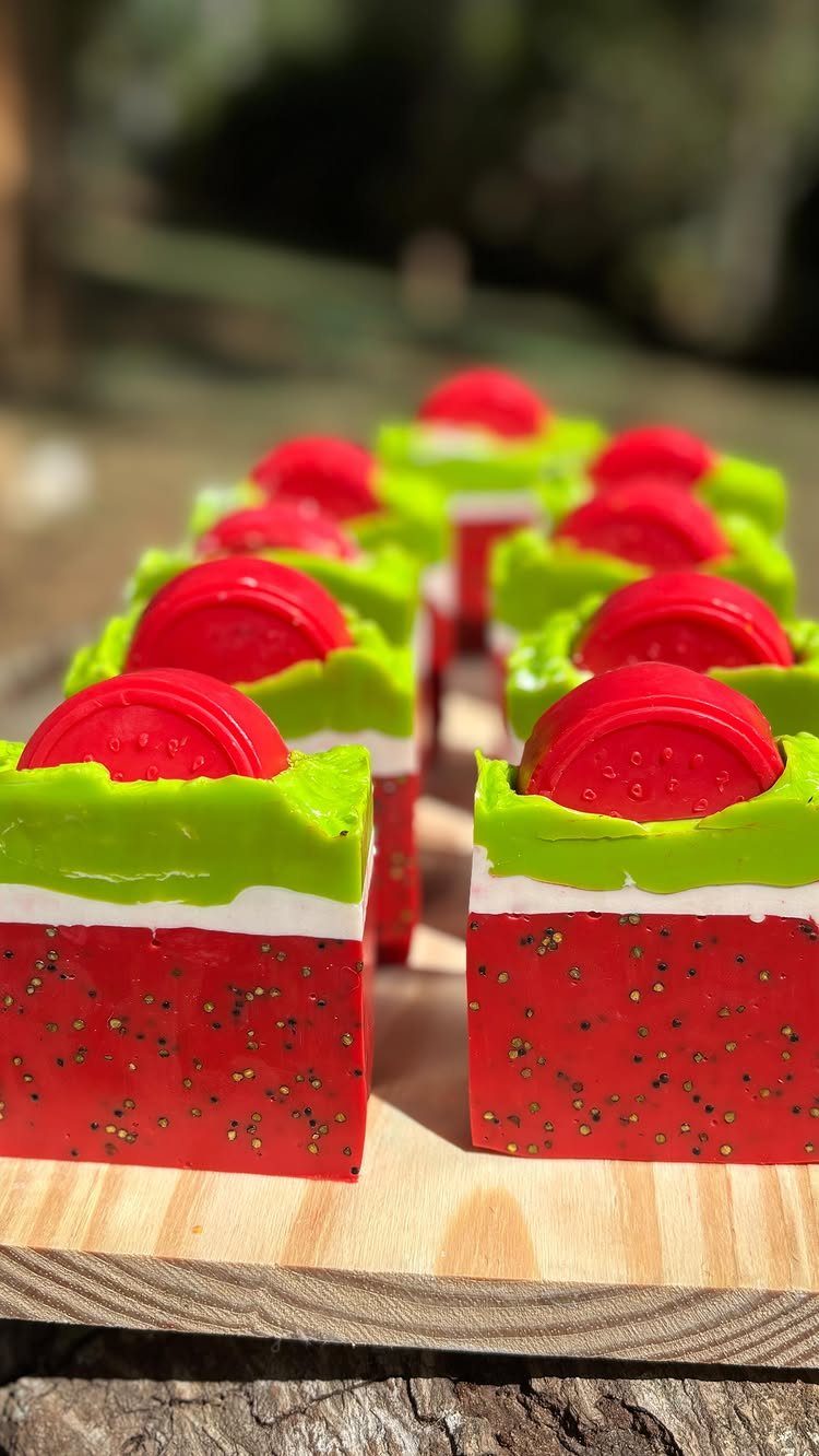 Watermelon-themed handmade soap bars arranged on a light wooden board outdoors.