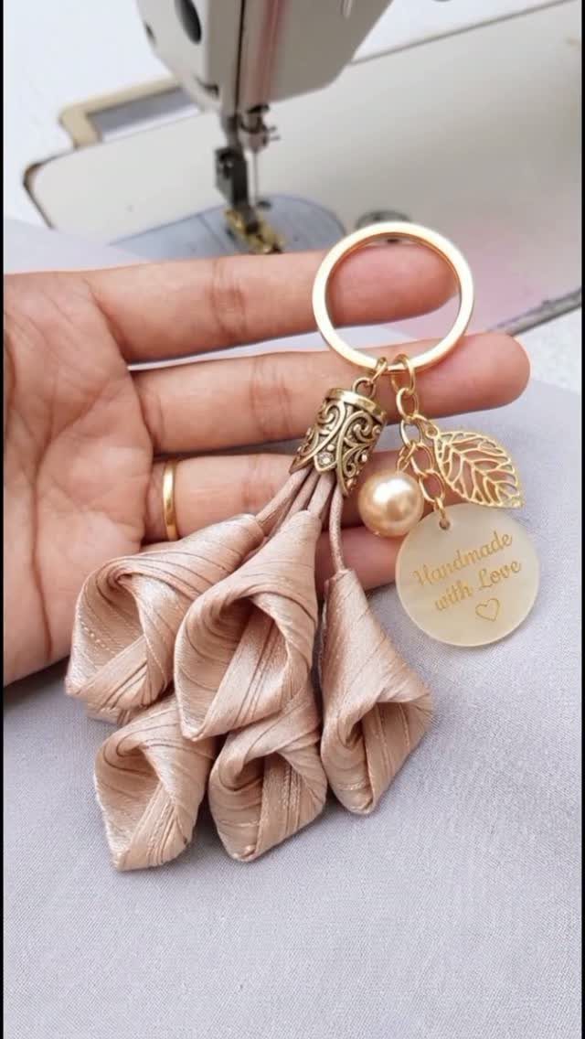 Champagne fabric tassel keychain with pearl and leaf charms held by a hand.