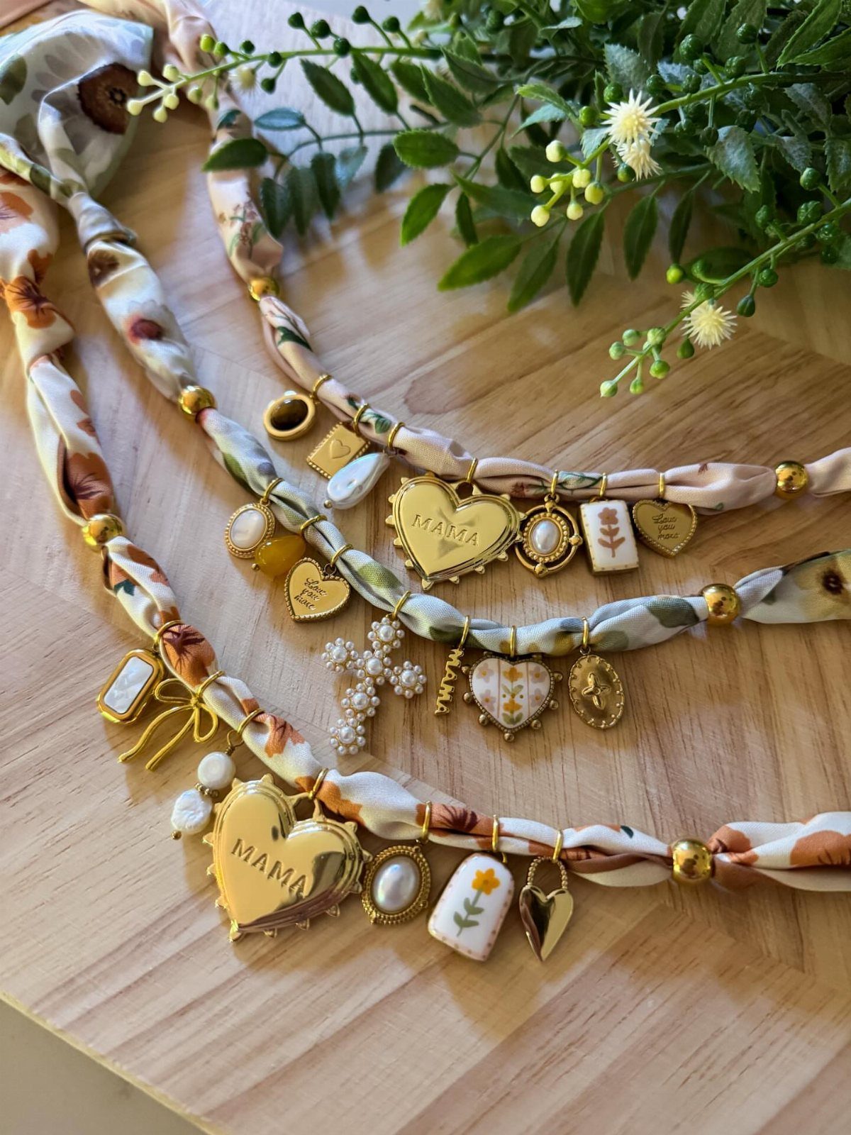 Fabric necklaces with gold MAMA heart charms and pearls on a wooden surface.
