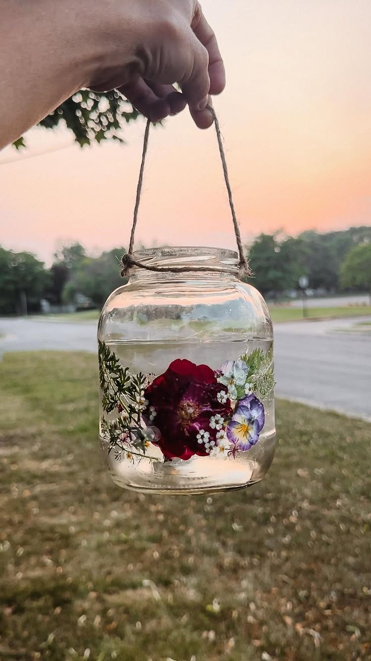 Glass jar with pressed red and purple flowers held by a twine string.
