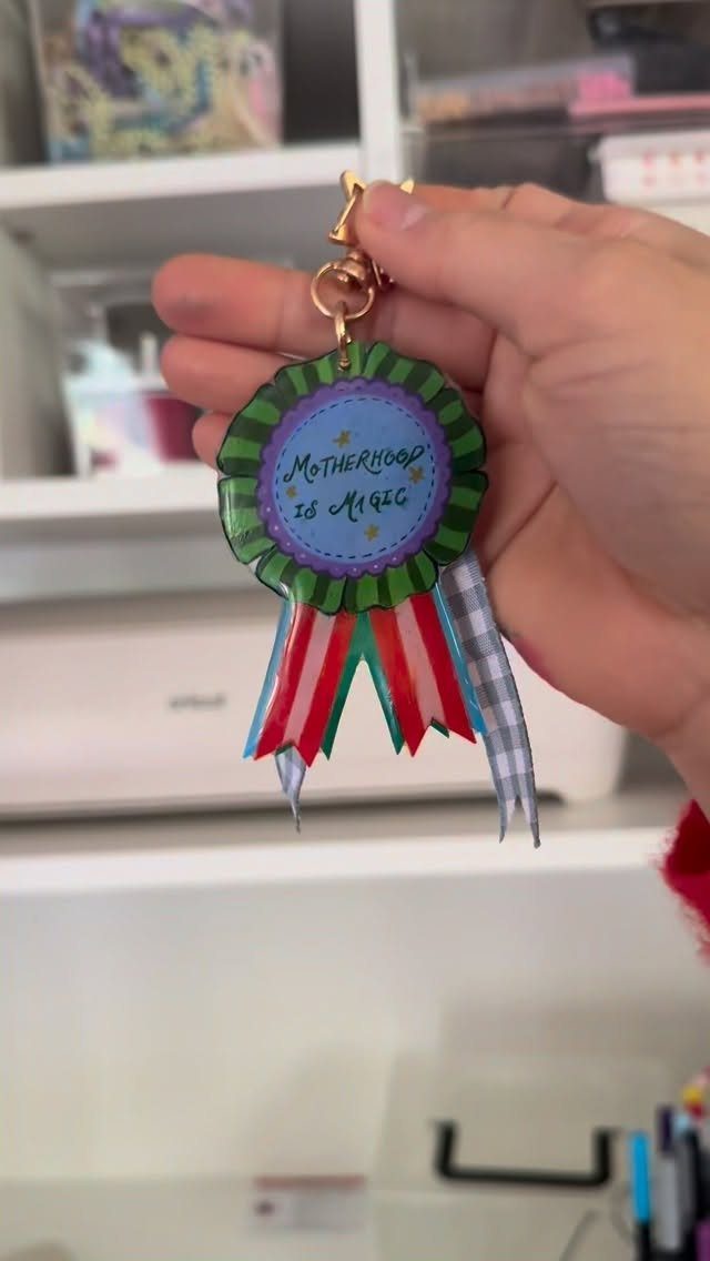 Handmade ribbon award keychain with text saying Motherhood is Magic held by hand.
