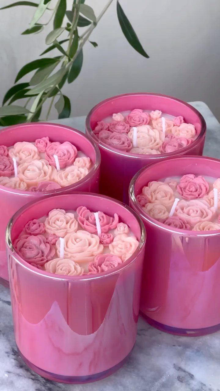 Pink rose-shaped candles in glass jars arranged on a marble surface.