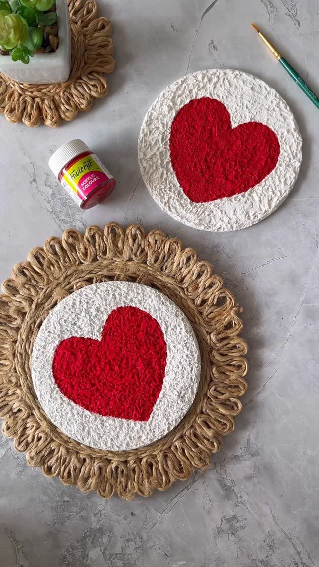 Two white textured coasters with red hearts on a grey stone surface.