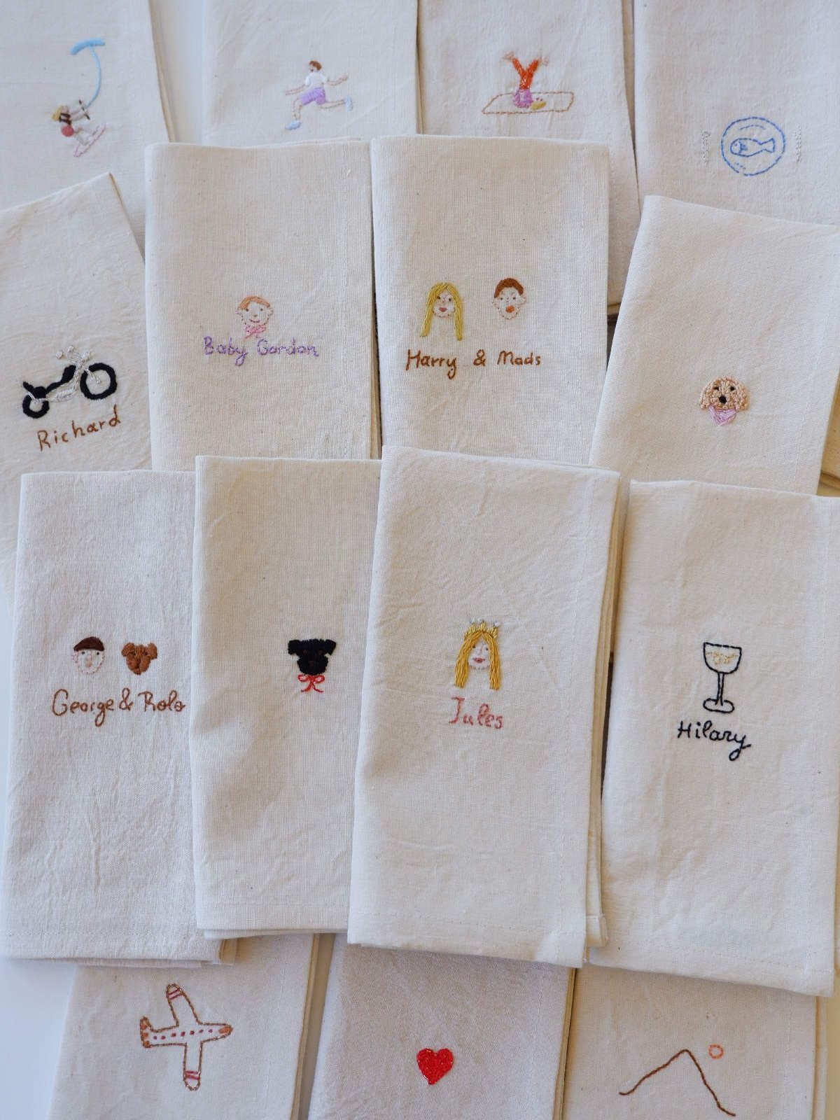 White embroidered dishtowels with personalized names and small colorful stitched illustrations.