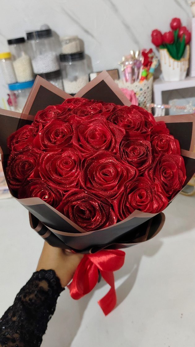 Glittery red rose bouquet wrapped in black paper held by a person.