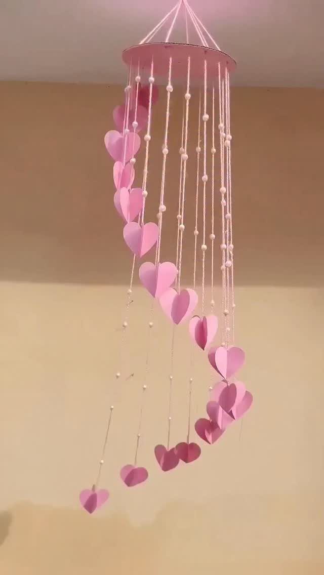 Pink heart-shaped wind chimes hanging from a circular base against a beige wall.