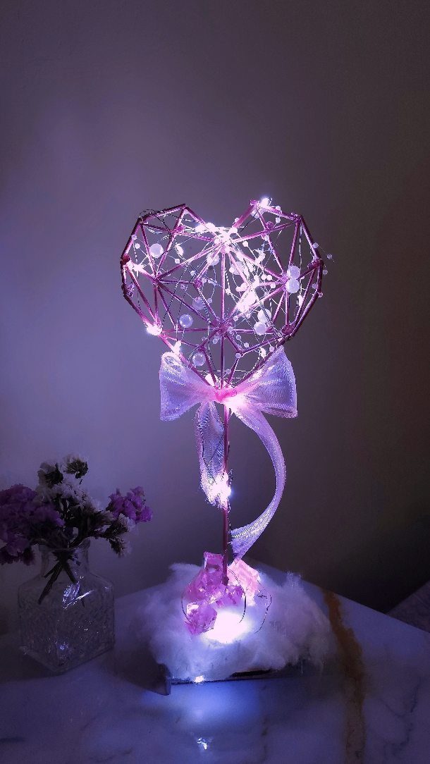 Heart-shaped wire sculpture with white fairy lights and a pink ribbon bow.