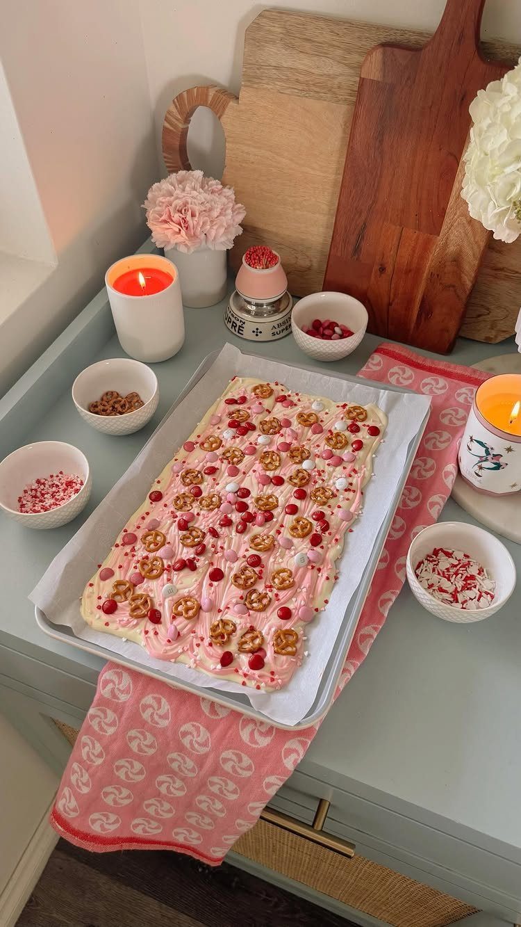 Pink frosted cake with berries and cookies on a baking sheet with toppings.