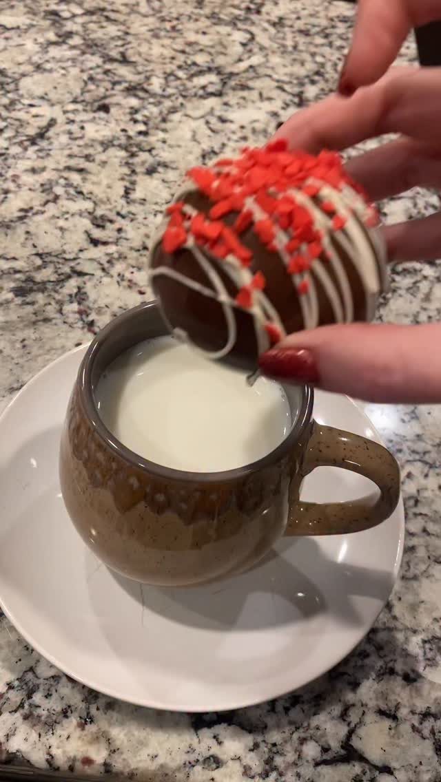 Chocolate bomb with red sprinkles held over a mug of warm milk