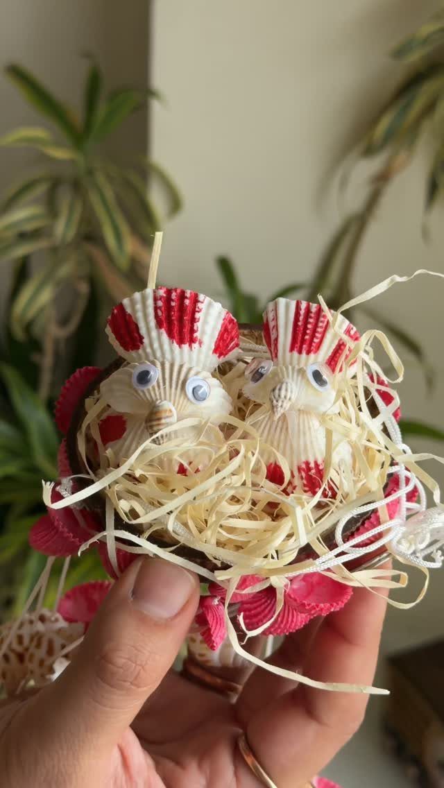 Seashell craft figures nestled in shredded paper held by a person's hand.