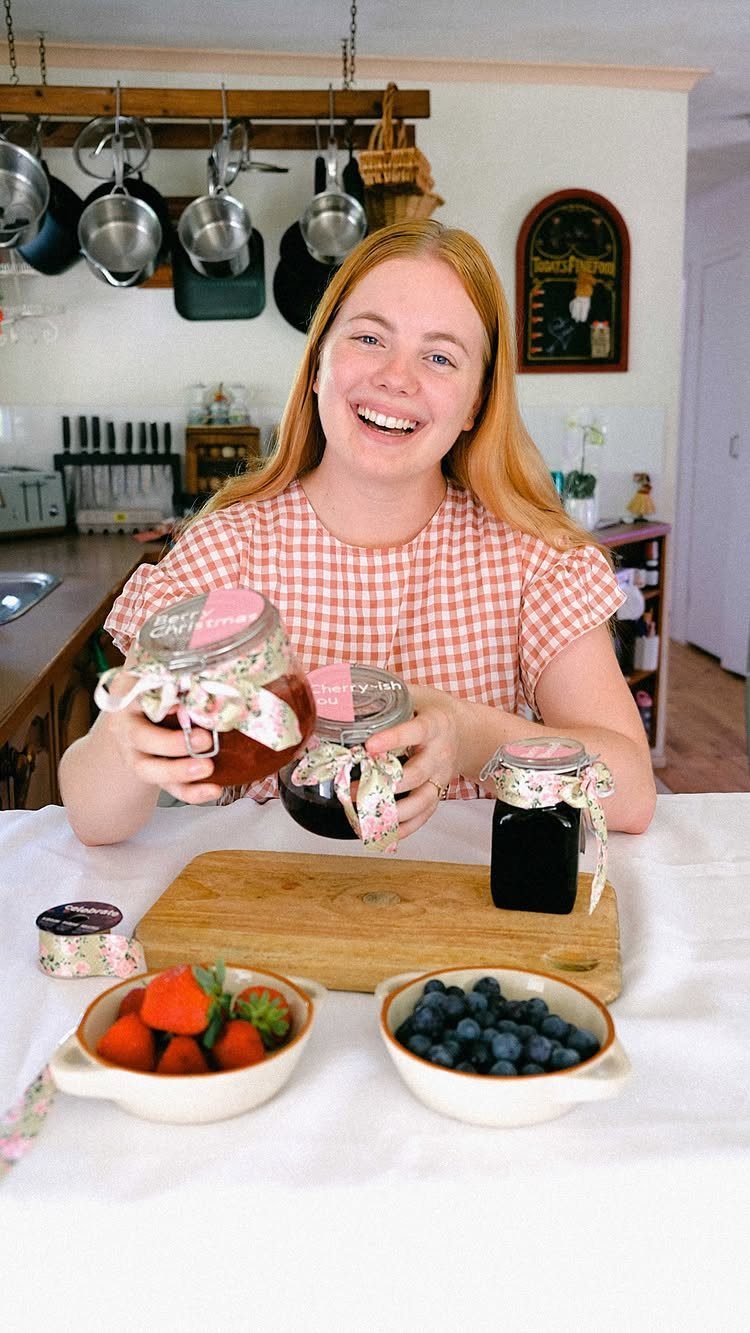 Woman holding homemade jam jars with berries on a table in a kitchen