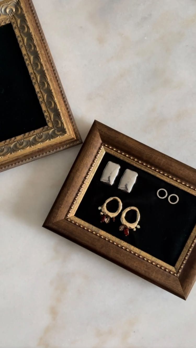 Gold ornate picture frame repurposed as a jewelry organizer holding rings and earrings.