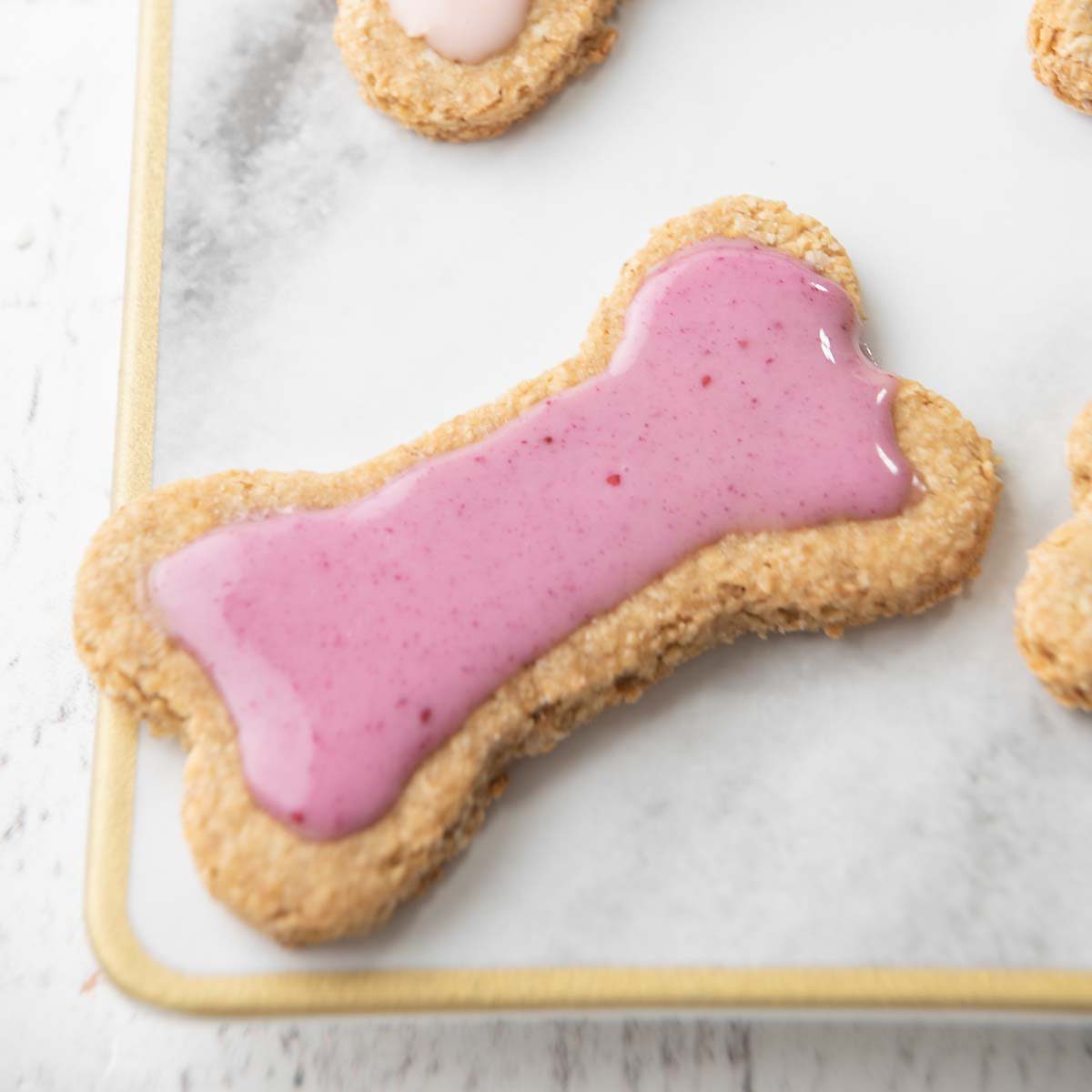 Bone-shaped dog biscuits topped with pink icing on a white baking sheet.