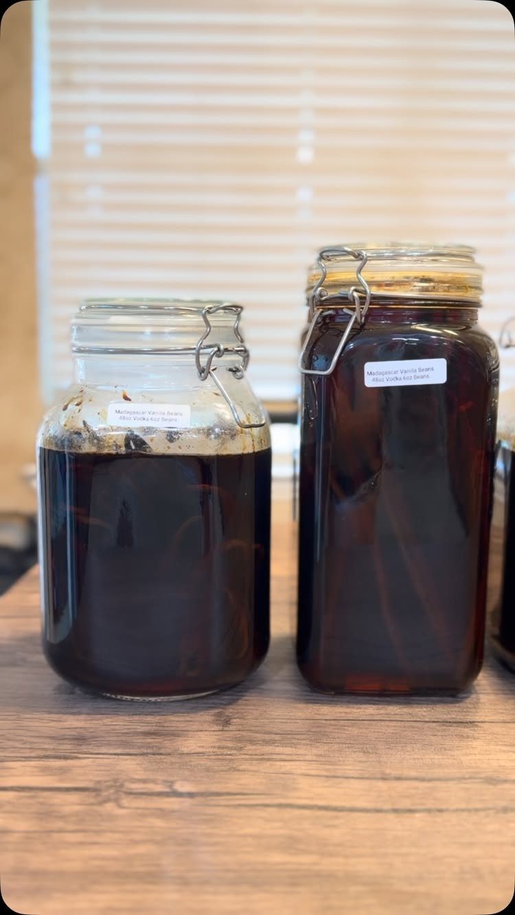 Two glass jars filled with dark vanilla extract and beans on wooden table