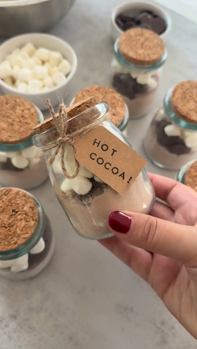 Hand holding a glass jar hot cocoa kit with layered ingredients and cork lid