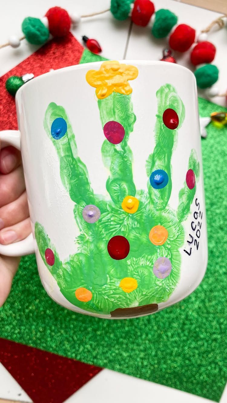 White ceramic mug with a green painted handprint and colorful dots.