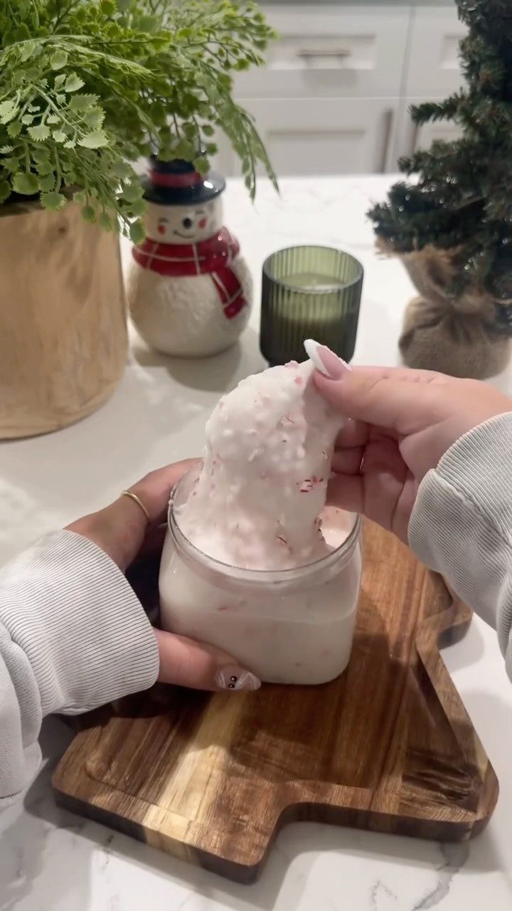 Hands lifting white grainy sugar scrub from a glass jar on wooden board