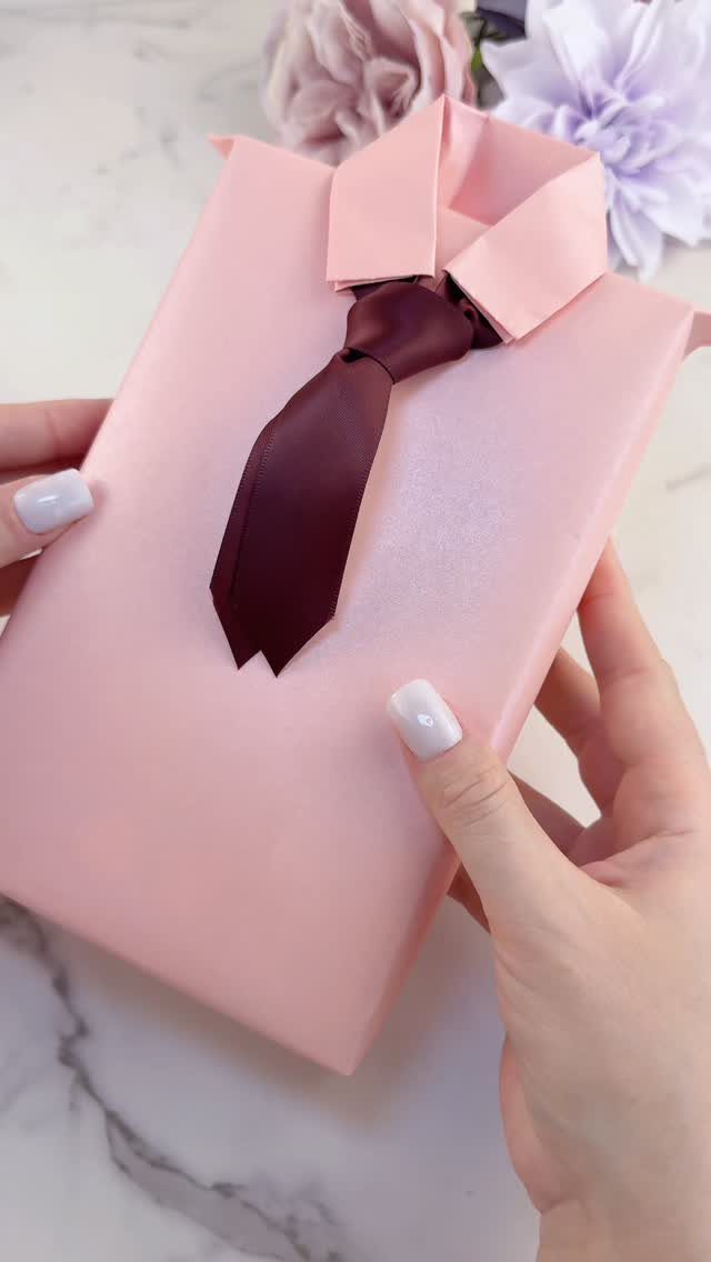 Pink gift wrapped as a dress shirt with a burgundy tie held by hands.