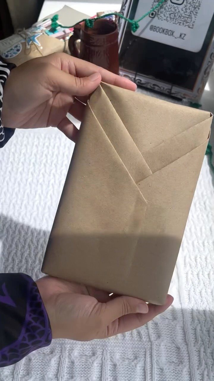 Hands holding a book wrapped in brown kraft paper with an envelope fold.