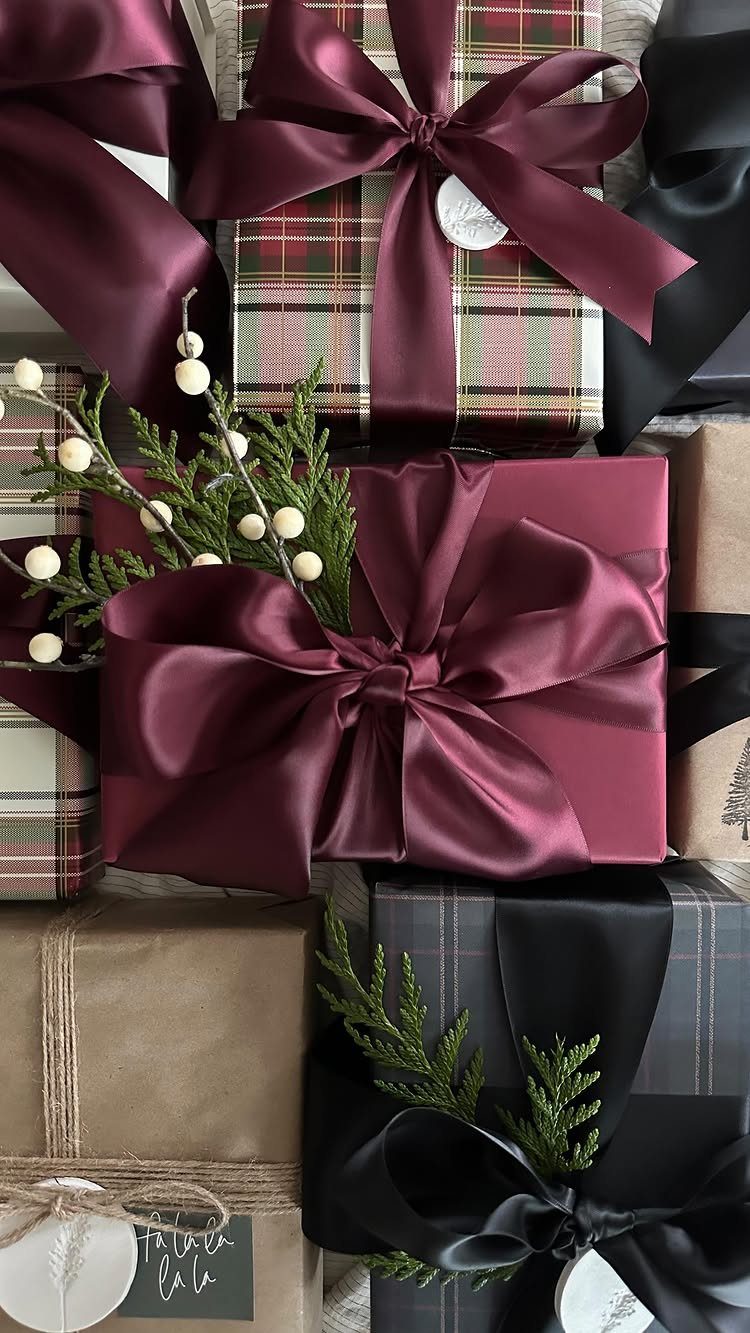 Wrapped gifts with burgundy and black satin ribbons and evergreen sprigs.