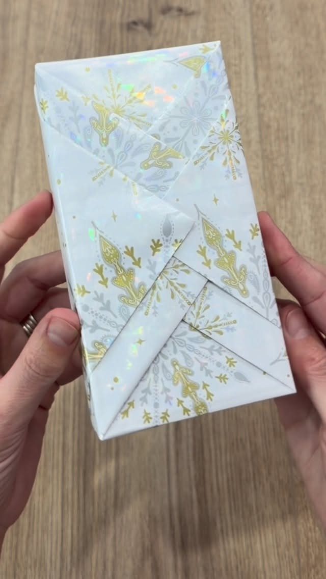 Hands holding a book wrapped in white and gold floral gift wrap.