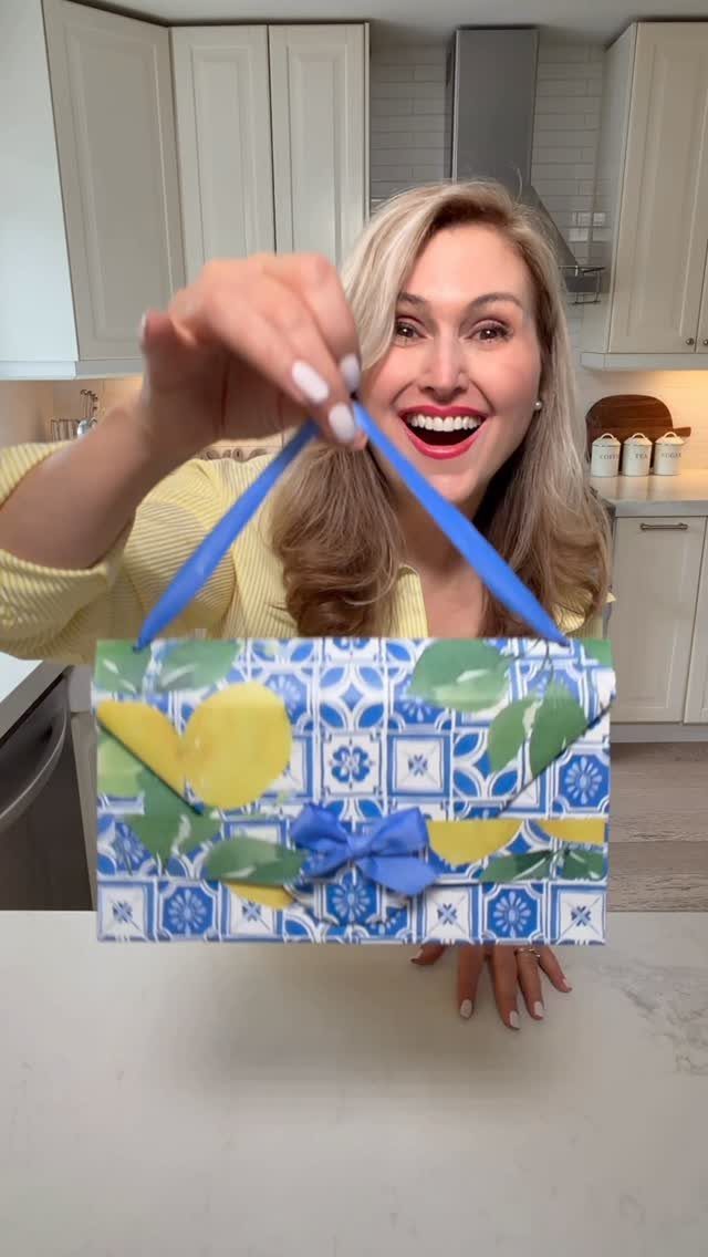 Handmade lemon-patterned wrapping paper gift bag with blue ribbon handles held by woman.