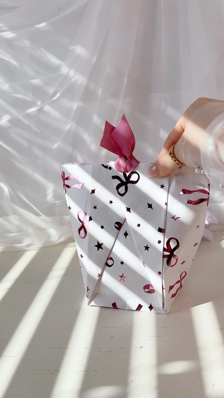 White patterned gift bag with pink ribbon handle on a white surface.