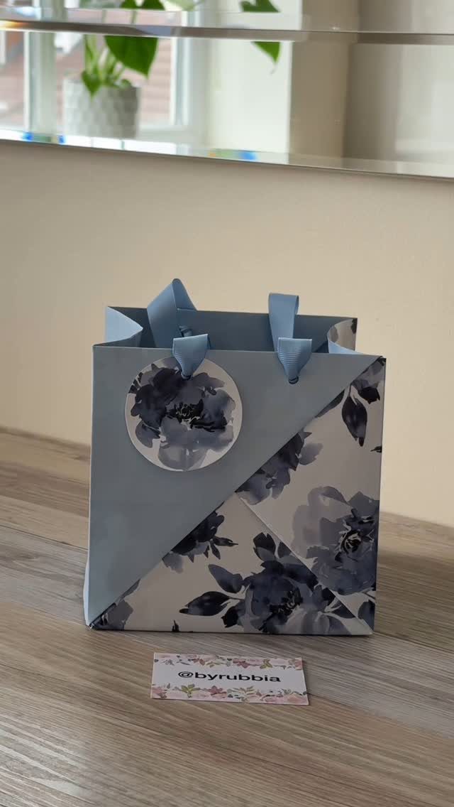 Blue floral gift bag with a diagonal triangular fold and ribbon handles.