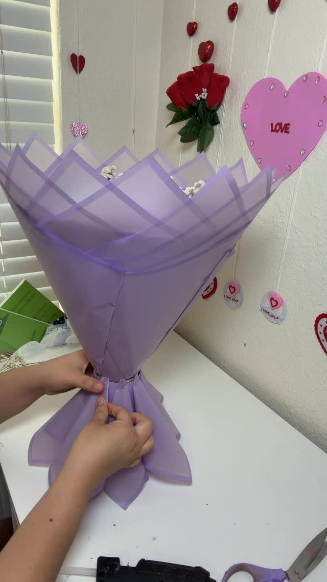Hands wrapping a flower bouquet in purple translucent paper on a white table